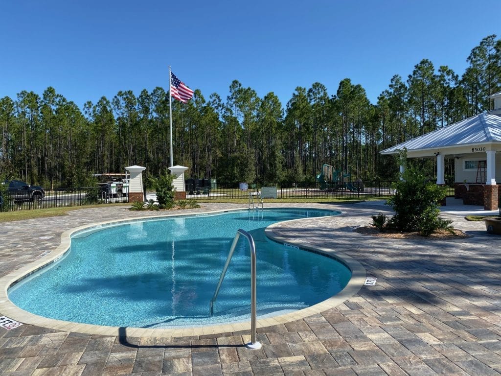 Community amenity center in Jacksonville by The Dänztler Group, featuring a commercial swimming pool, extensive paver deck, and surrounding recreational facilities. Expert HOA and developer contractor.